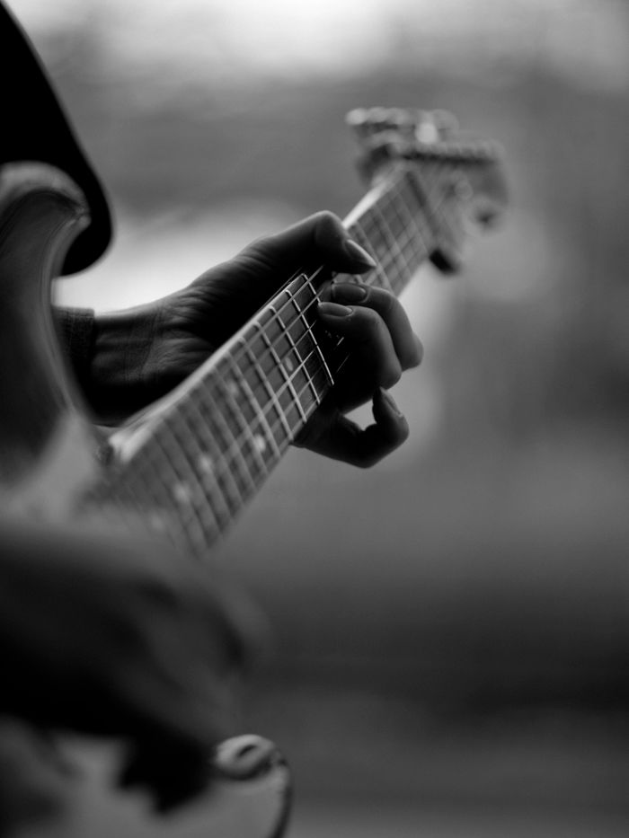 Black-and-white close-up of a person playing an electric guitar, focusing on the frets.